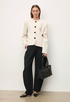 Krémovo sfarbené štruktúrované sako s čiernymi gombíkmi, kombinované s čiernymi širokými nohavicami a čiernou tkanou kabelkou. Čierne lodičky so špicatou špičkou.