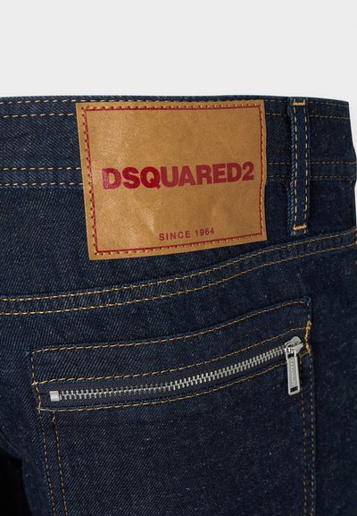Σκούρο μπλε τζιν από denim με καφέ δερμάτινη ταμπέλα που αναγράφει "DSQUARED2" και "SINCE 1964", με κίτρινη ραφή και ασημένια τσέπη με φερμουάρ.