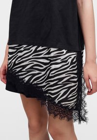 Φούστα με ασπρόμαυρο σχέδιο ζέβρας με μαύρη δαντέλα, φορεμένη κάτω από μαύρο τοπ, που δείχνει το κάτω μέρος του κορμού και το επάνω μέρος των ποδιών.