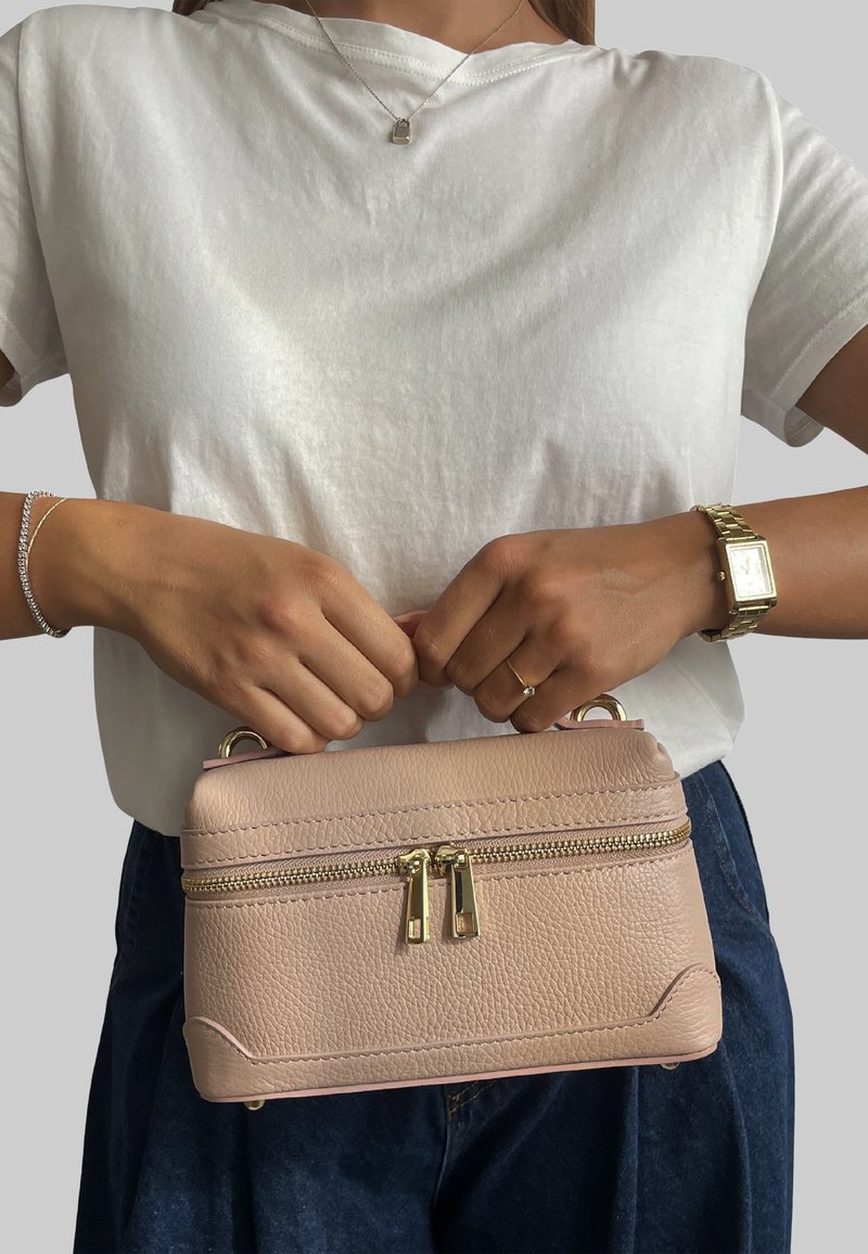 Różowa torba skórzana w odcieniu blush z teksturowanym wykończeniem, złotymi akcesoriami i podwójnym zapięciem na zamek. Kompaktowy prostokątny kształt z górnymi uchwytami.