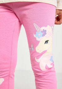 Lyserøde leggings i blød bomuld med et enhjørningmotiv, der indeholder blomster og sommerfugle. Glat tekstur, slankt design, levende farver.