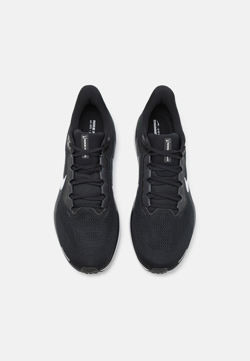 Zapatillas deportivas negras con una parte superior de malla texturizada, cordones planos negros y acentos blancos en los lados y el talón. Diseño ligero y aerodinámico.