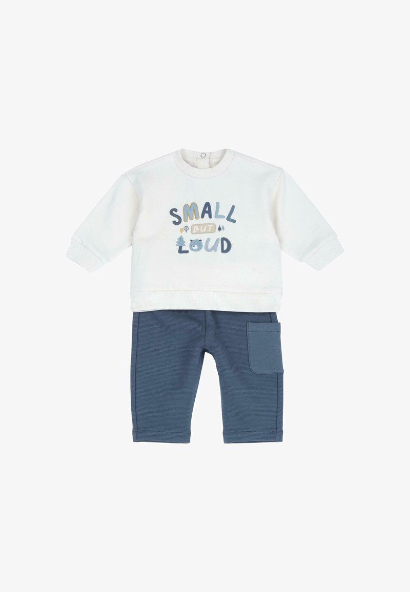 T-shirt blanc à manches longues pour bébé avec le texte « PETIT MAIS BRUYANT » et pantalon bleu avec poche latérale, tous deux en tissu doux.