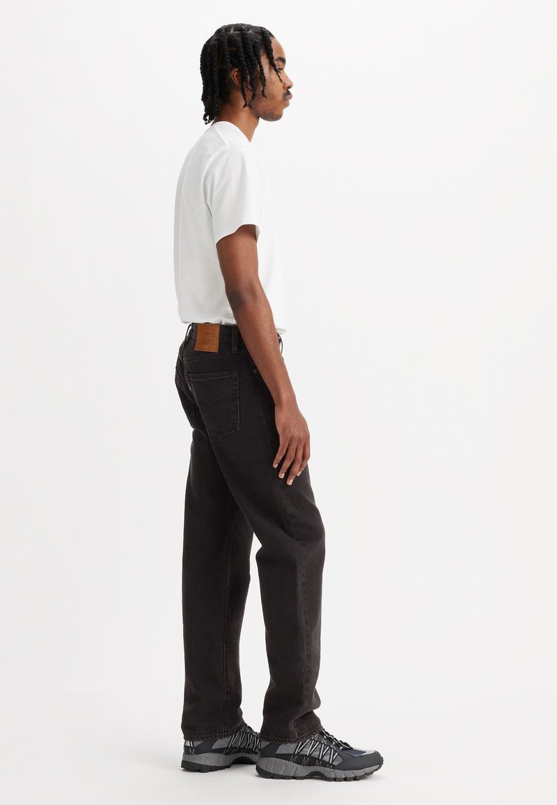 Zwarte denim jeans met een rechte snit, gecombineerd met een wit T-shirt. Zwart en grijs sneakers met een textuurontwerp. Bruin leren patchdetail.