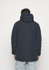 Granatowa pikowana kurtka z odpinanym kapturem, z wysokim kołnierzem, długimi rękawami i bocznymi kieszeniami. Gładka tekstura i opływowy fason.