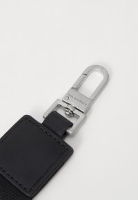 Cinturino in pelle nera con una clip in metallo argentato. Presenta un'applicazione rettangolare in pelle e un marchio inciso sull'hardware. Texture liscia.