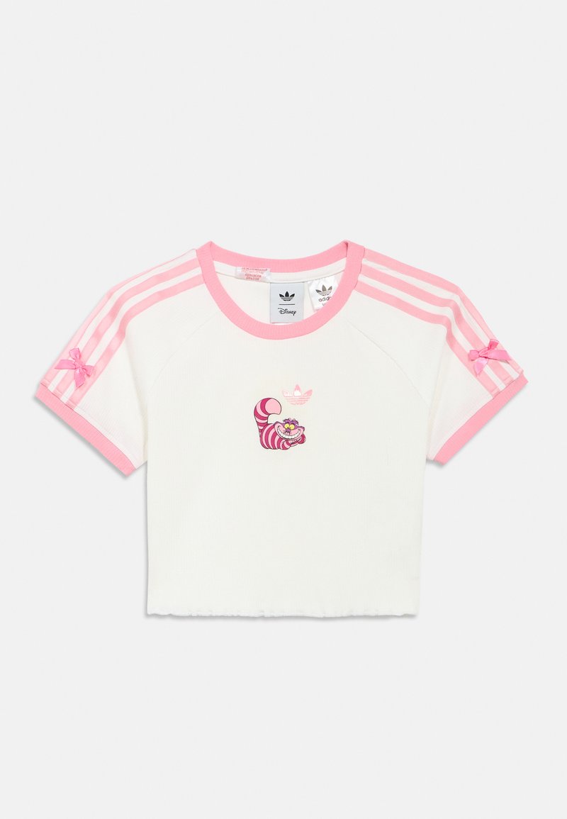 Fehér, felülvágott póló rózsaszín díszítésekkel, amelyen egy Cheshire macska grafika és rózsaszín Adidas csíkok találhatók a vállakon. Pamut anyagból.