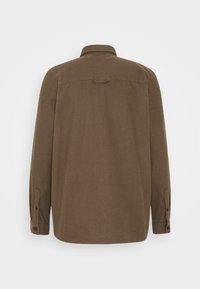 Chemise marron avec col, manches longues, poignets à boutons et une seule pièce de cape au dos. Texture de tissu lisse sans motifs visibles.