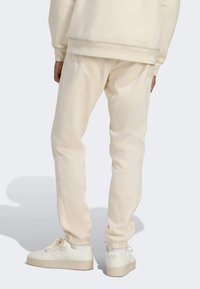 Sweat-shirt et pantalon de survêtement couleur crème en tissu doux avec poignets élastiques, assortis à des baskets blanches avec trois bandes et une semelle compensée.