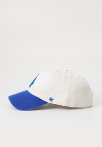 Căciulă de baseball cu un corp din bumbac de culoare crem și vizieră albastră. Prezintă un logo brodat și marca pe lateral. Curea ajustabilă la spate.