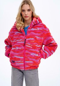 Puchata, kapturowa kurtka z falistym wzorem w odcieniach ró�żu i fioletu, z zamkiem błyskawicznym z przodu i elastycznymi mankietami. Miękka tekstura.
