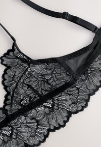 Must pitsist pitsist pesuga rinnahoidja, millel on keerukad lillemustrid, lainelised servad, reguleeritavad rihmad ja võrgust vooder, lisades tekstuuri ja detaile.