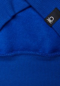 Sudadera azul con un interior suave y texturizado y un cuello acanalado. Incluye una etiqueta negra con un acento de logo blanco.