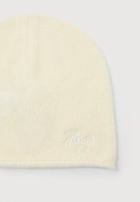 Kremowa, dziana czapka z delikatnym prążkowaniem i małym, haftowanym logo "Hugo" w białej nitce blisko dolnej krawędzi.