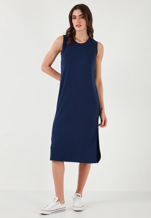 Navy sleeveless dress with a straight cut and side slit, made of soft fabric. Paired with white sneakers for a casual look.