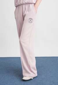 Lyserøde svedbukser med elastisk talje, sidelommer og et cirkulært "Paris" logo på venstre lår. Glat tekstur, loose fit.