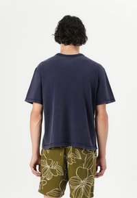 Navy blue, short-sleeve t-shirt with a relaxed fit, round neckline, and a soft, slightly textured fabric. Worn with patterned olive green shorts.