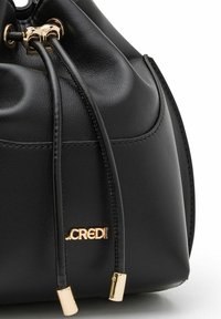 Bolso tipo cubo de cuero negro con textura suave, cierre de cordón, acentos de herrajes dorados y un logotipo en la parte frontal.