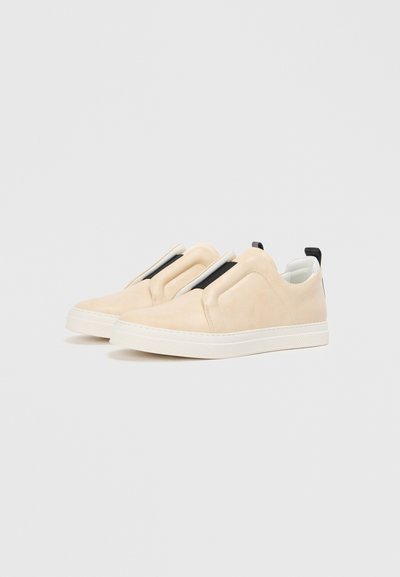 Sneakers slip-on bej cu un finisaj neted din suede, având o talpă din cauciuc alb și accente elastice negre. Design minimalist cu formă rotunjită.
