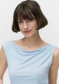 Ljusblå ärmlös topp med draperad halsringning, slät tygkvalitet och subtil lyster; har en avslappnad passform och minimalistisk design.