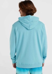 Felpa leggera blu con cappuccio regolabile, maniche lunghe e polsini a coste. Texture liscia. Indossata con pantaloni da bagno a righe.