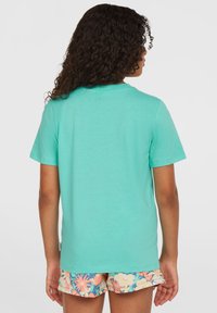 Mėlynas medvilninis trumpomis rankovėmis T-shirt su apvalia kaklo iškirpte ir laisvu kirpimu, derinamas su gėlių raštais dekoruotais šortais.
