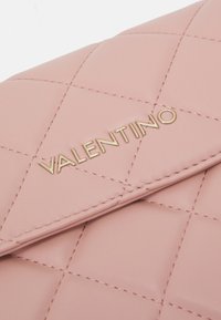 Patchwork šviesiai rožinės spalvos odinė rankinė su auksiniu "VALENTINO" logotipu, sudėtingais siūlėmis ir užlenkiama užsegimo dangteliu.