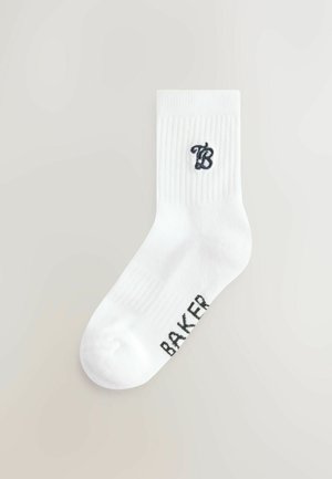 Hvid bomuldsstrømpe med ribbet tekstur, der har et lille sort "B" logo øverst og ordet "BAKER" i sort ved foden.