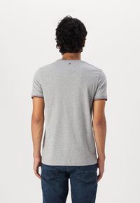 Lyhythihainen harmaa T-paita, jossa on ribbireunus ja punaiset sekä siniset yksityiskohdat; tasakudottu kangas, klassinen istuvuus, logopatchi selässä.