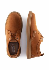 Zapatos de ante marrón con punta redonda, detalles de costura y ojales de metal para los cordones. Suela de goma flexible. Diseño casual.