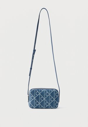 Mala pravokutna plava torbica preko tijela s podesivim remenom i geometrijskim uzorkom, visi na jednostavnoj svijetloj pozadini.