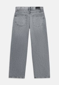 Pohled zezadu na šedé džíny s rovnými nohavicemi, dvěma zadními kapsami, poutky na pásek a černou koženou nášivkou na pasu.