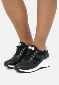 Scarpe sportive nere con tessuto testurizzato, accenti dorati e design con lacci, dotate di suola imbottita e un leggero tacco a cuneo.