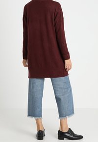 Burgundyröd långtröja med ribbade detaljer, parat med ljusblå avklippta jeans med fransade fållar och svarta läderskor.