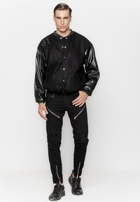 Czarna kurtka bomberka z błyszczącymi czarnymi skórzanymi rękawami, z zatrzaskami, w połączeniu z czarnymi spodniami z zamkami błyskawicznymi i slim fit. Czarne sneakersy.