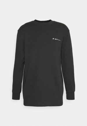 Pika, musta pikkade varrukatega T-särk, mis on valmistatud puuvillast, koos ümmarguse kaelusega ja väikese valge logoga vasakul rinnapiiril. Sile tekstuur.