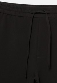 Pantalons noirs à taille élastique avec cordon de serrage, présentant une texture lisse et un design simple, sans fermetures ni embellissements visibles.