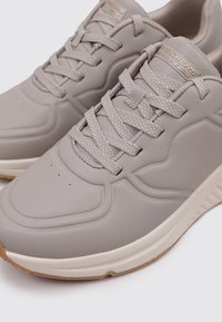 Zapatillas deportivas grises de cuero texturizado, con punta redonda, cierre de cordones y suela de goma ligera con acentos en color marrón.