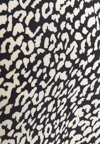 Un tissu noir exhibe un motif abstrait ressemblant à celui d'un léopard blanc, avec des formes irrégulières et des tailles variées, créant une apparence texturée.