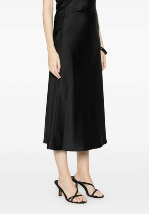 Donna che indossa una gonna midi in raso nero abbinata a sandali neri con tacco e cinturini, in piedi con le braccia rilassate ai lati.