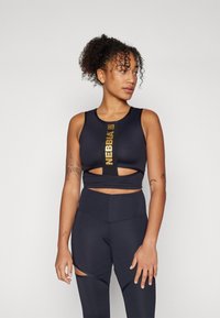 Crni sportski crop top s izrezima, sa zlatnim logotipom "NEBBIA". Uparen s visokim tajicama, također crnim, s detaljima izreza.