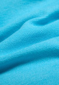 Nahaufnahme eines hellblauen, strukturierten Stoffes mit kleinem Strickmuster und sanften Falten.