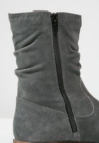 Bottine en suédine grise avec un design décontracté, dotée d'une fermeture éclair sur le côté et de coutures contrastantes le long de la semelle. Texture lisse et bout arrondi.