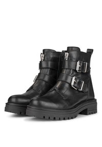 Botas de cuero negras hasta el tobillo con dos cremalleras laterales y tres hebillas de plata ajustables. Suela de goma resistente con un patrón de dibujo texturizado.