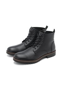 Botas de cuero negro hasta el tobillo con punteras redondas, suelas planas y seis ojales para los cordones. Presentan un acabado texturizado y un acento marrón en la suela.