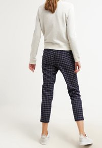 Tmavě modré kárované kalhoty s úzkým střihem, zkrácenou délkou a elastickým pasem, kombinované s světle šedým svetrem a bílými teniskami.