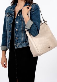 Beżowa pleciona torebka o gładkiej fakturze, z akcentem ze srebrnego metalu. Noszona z niebieską kurtką dżinsową na czarnej sukience.
