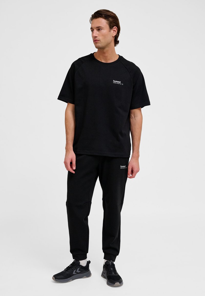 Svart kortärmad t-shirt med raglanärmar, parat med svarta joggingbyxor. Båda har en liten logotypdetalj på bröstet och benet.