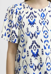 Blusa a maniche corte in tessuto crema chiaro con un audace motivo floreale astratto blu e navy, dettagli con spalle arricciate e scollatura rotonda.