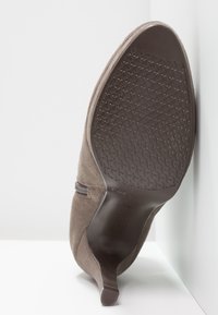 Stivale alla caviglia in suede marrone con suola in gomma testurizzata e punta affusolata, dotato di cerniera laterale per una facile vestibilità.